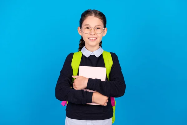Foto van goed humeur glimlachende intelligente schoolmeisje dragen rugzak knuffel boek materialen geïsoleerd op blauwe kleur achtergrond — Stockfoto