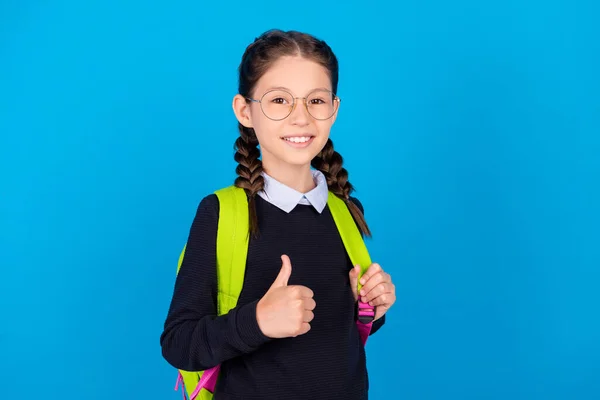 Foto de bastante cura pequeña chica feliz mostrar pulgar arriba usar gafas mochila inteligente aislado sobre fondo de color azul — Foto de Stock