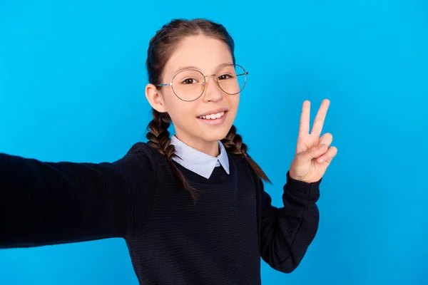 Fotografie roztomilé šťastný hezká školačka dobrou náladu, aby selfie show V-sign izolované na modrém pozadí — Stock fotografie