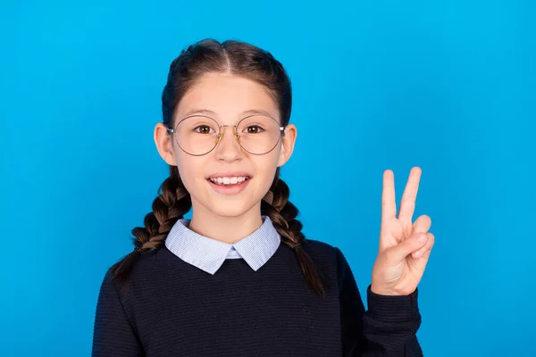 Foto de sorrindo bom humor bela estudante inteligente mostrando v-sinal desgaste óculos isolados no fundo de cor azul — Fotografia de Stock