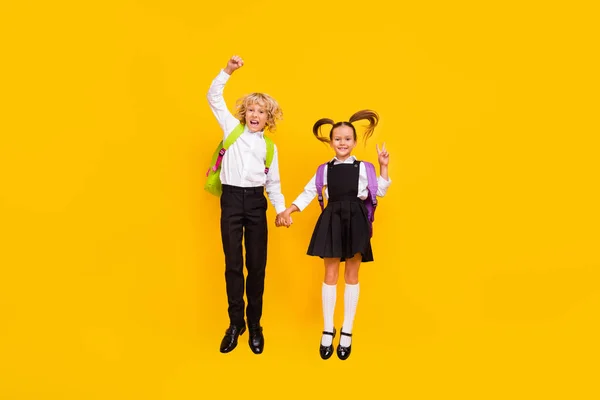 Foto von verrückten Kindern springen halten Hände zeigen Siegeszeichen tragen Schuluniform isoliert gelbe Farbe Hintergrund — Stockfoto