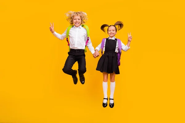 Foto av sportiga glada barn hoppa grepp händer visa v-tecken slitage skola uniform isolerad gul färg bakgrund — Stockfoto