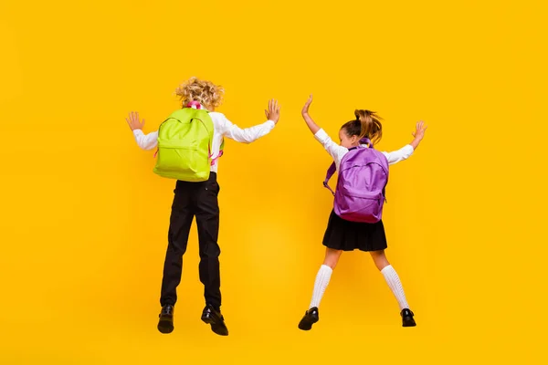 Parte posterior trasera ver foto de divertido positivo niños salto desgaste mochila escuela uniforme aislado amarillo color fondo —  Fotos de Stock
