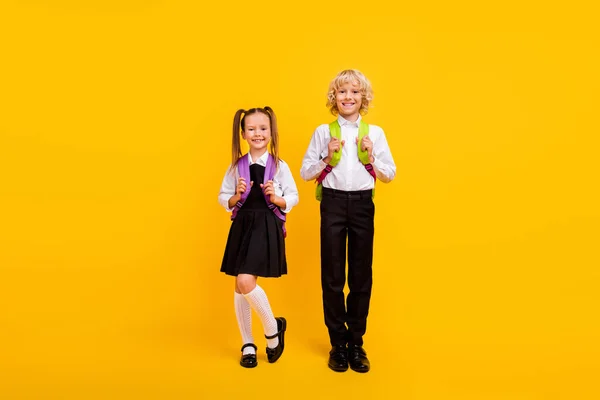 Фото гарних щасливих школярів, які позують носіння рюкзака шкільної форми ізольованого жовтого кольору фону — стокове фото