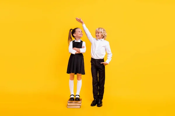 자신감 있는 여학생이 남아 있는 사진 파일 책 소년의 높이 측정 학교 유니폼외진 노란색 배경을 착용 — 스톡 사진