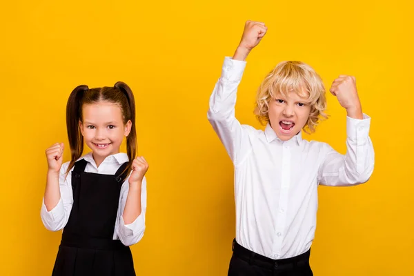 Foto de dos escolares asombrados celebran victoria usan uniforme escolar aislado color amarillo fondo —  Fotos de Stock