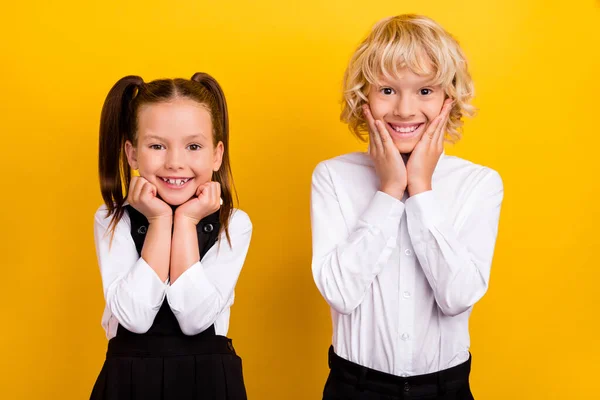 Foto de dos compañeros de clase colegiales manos mejillas sonrisa dentada llevar uniforme escolar aislado color amarillo fondo —  Fotos de Stock