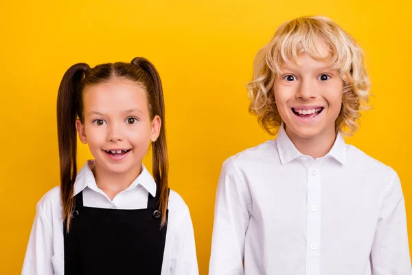 Foto de dos escolares positivos divertidos brillante sonrisa blanca usar uniforme escolar aislado color amarillo fondo — Foto de Stock