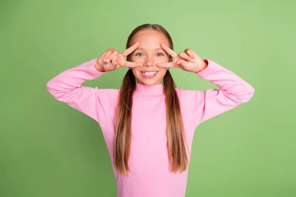 Retrato de chica alegre atractiva mostrando v-signo cerca de ojo divertirse aislado sobre fondo de color verde brillante — Foto de Stock