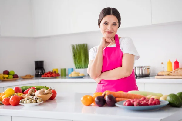 Foto de adorable dama joven reflexiva usar delantal rosa mano barbilla cocina cena sonriente interior habitación casa —  Fotos de Stock