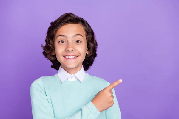 Фото солодкого привабливого шкільного хлопчика носити сльозогінний пуловер, що вказує на порожній простір, усміхнений ізольований фіолетовий кольоровий фон — стокове фото