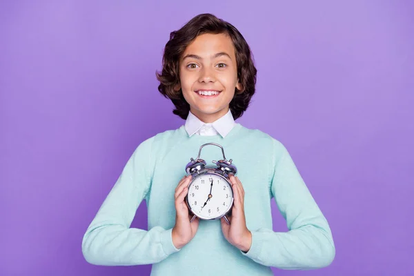 Foto von kleinen fröhlichen brünetten Jungen halten Uhr tragen blauen Pullover isoliert auf lila Hintergrund — Stockfoto