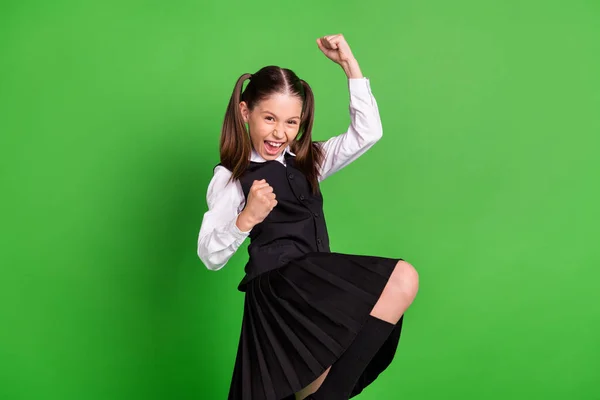Foto de la divertida chica de la escuela de la suerte usar negro blanco uniforme levantando puños sonriendo aislado color verde fondo —  Fotos de Stock