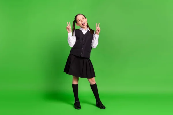 Foto di affascinante studentessa ingannevole vestito bianco nero uniforme sorridente mostrando lingua v-segno isolato colore verde sfondo — Foto Stock