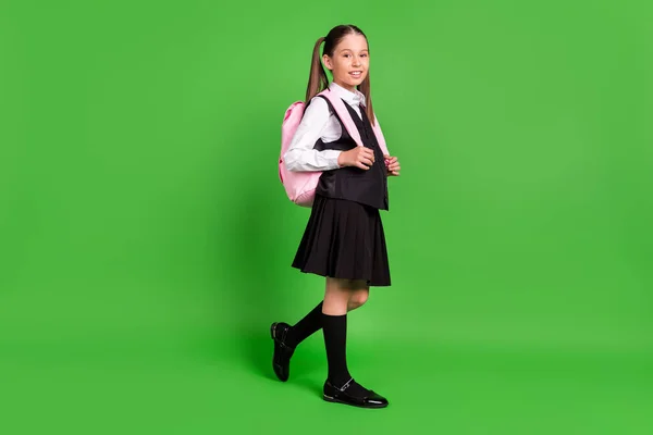 Foto de linda adorable niña de la escuela usar negro blanco uniforme mochila caminando sonriente aislado color verde fondo — Foto de Stock