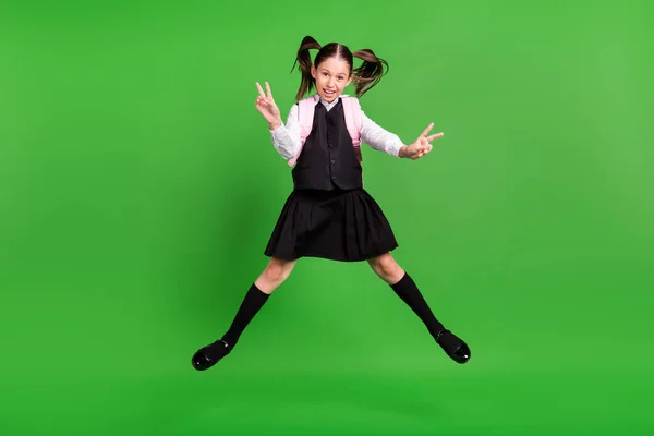 Photo positive écolière mignonne habillée blanc uniforme sac à dos sautant haut montrant v-signes isolé fond de couleur verte — Photo
