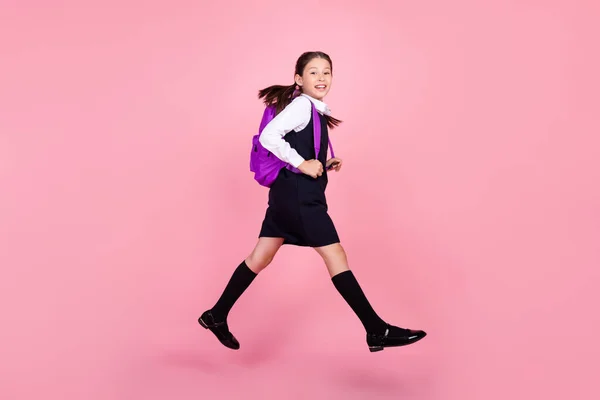 Full längd kropp storlek foto skolflicka hoppa upp med ryggsäck promenader till skolan isolerad pastell rosa färg bakgrund — Stockfoto