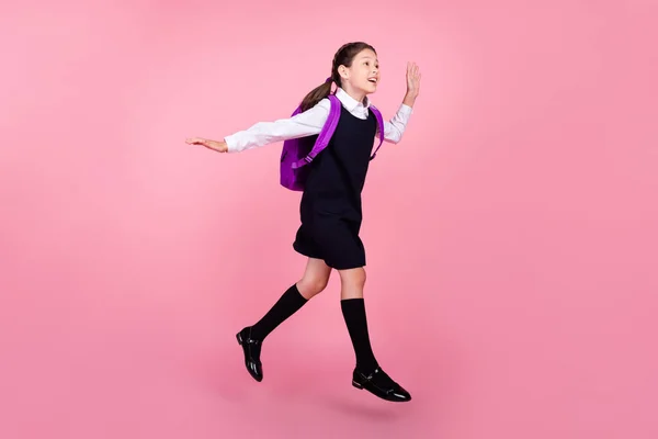 Фотография школьницы в полный рост, прыгающей на уроке с протянутой рукой на фоне розового цвета — стоковое фото