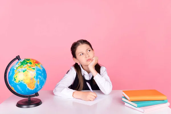 Foto porträtt liten flicka med svansar sitter vid skrivbordet skriva examen tankeväckande övervägda isolerade pastell rosa färg bakgrund — Stockfoto