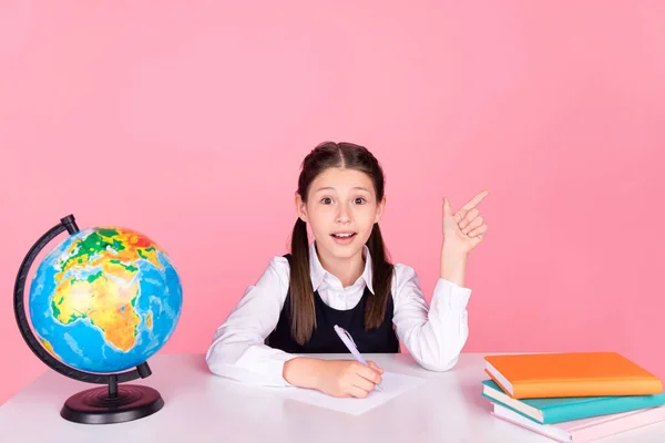 Photo portrait little girl with tails sitting at desk writing exam showing copyspace isolated pastel pink color background — Stock Photo, Image