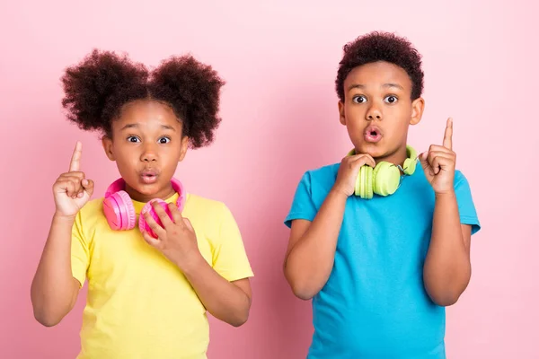 Retrato de dos amigos divertidos atractivos sorprendidos amistad escuchar melodía apuntando hacia arriba aislado sobre fondo de color rosa —  Fotos de Stock