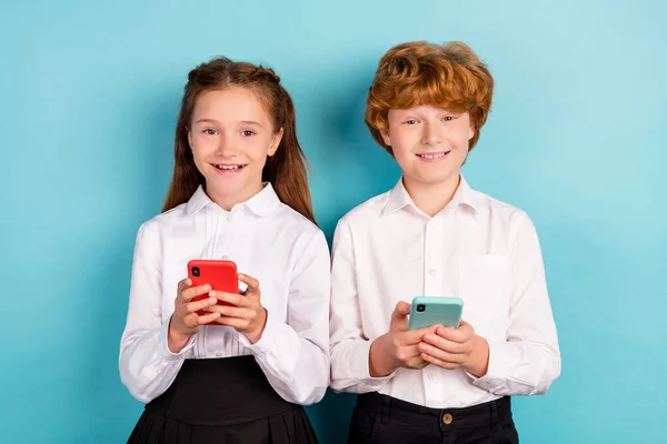 Retrato de dos atractivos niños alegres utilizando dispositivo gadget aplicación 5g smm aislado sobre fondo de color azul brillante —  Fotos de Stock