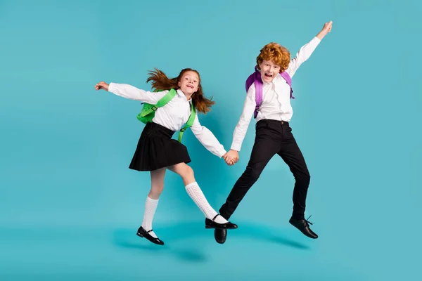 Фото двох божевільних школярів, які тримають стрибок рук, носять білу сорочку уніформу ізольованого синього кольору фону — стокове фото