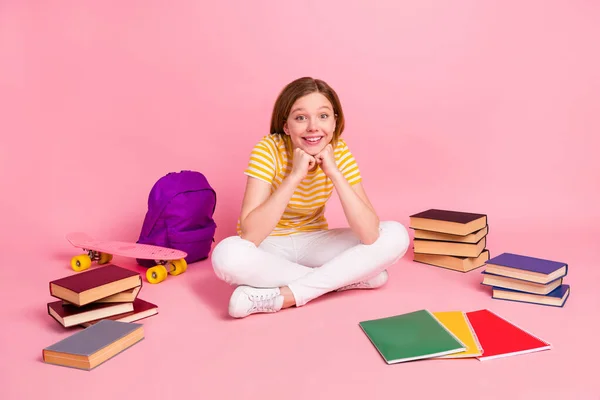 Fotografie pozitivní roztomilé dívka sedět na podlaze připravit domácí práce nosit pruhované žluté tričko izolované růžové barvy pozadí — Stock fotografie