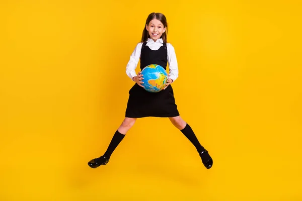Volledige lengte lichaam grootte foto klein schoolmeisje springen houden globe op school geïsoleerde levendige gele kleur achtergrond — Stockfoto