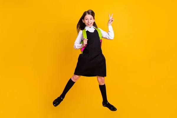 Foto de cuerpo completo de la niña pequeña de pelo marrón saltar hacer v-signo de desgaste bolsa aislada en el fondo de color amarillo —  Fotos de Stock