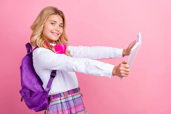 Foto van glanzende mooie school meisje gekleed formele kleding rugzak oortelefoons glimlachend lezen boek geïsoleerde roze kleur achtergrond — Stockfoto