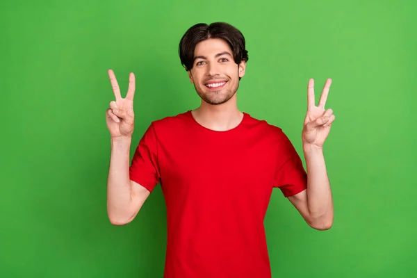 Foto von gut aussehenden fröhlichen Kerl zeigen zwei V-Zeichen strahlendes Lächeln tragen rotes T-Shirt isoliert grüne Farbe Hintergrund — Stockfoto
