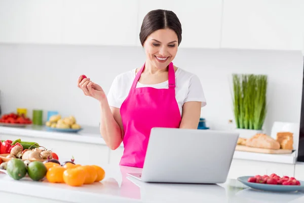 Φωτογραφία από χαριτωμένα καστανά μαλλιά νεαρή κοπέλα ρολόι φορητό υπολογιστή μάγειρας από το σπίτι φορούν λευκό t-shirt ποδιά στην κουζίνα — Φωτογραφία Αρχείου
