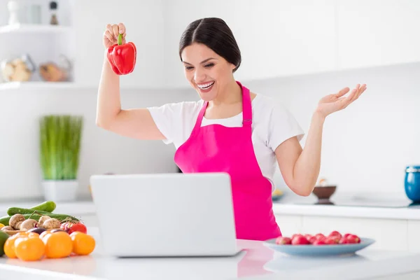 Φωτογραφία της γοητευτικής ενθουσιασμένοι γυναίκα ντυμένος ροζ ποδιά χαμογελώντας μαγείρεμα γεύμα βλέποντας σύγχρονη συσκευή σε εσωτερικούς χώρους σπίτι δωμάτιο — Φωτογραφία Αρχείου
