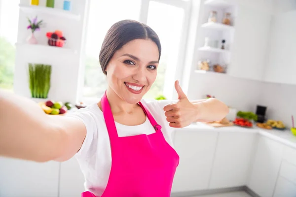 Foto van grappige mooie jonge dame dragen roze schort koken diner spijkeren selfie tonen duim omhoog glimlachen binnen kamer huis — Stockfoto