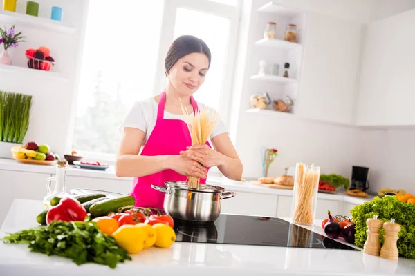 Zdjęcie optymistycznej brunetka millenium pani gotować makaron nosić fartuch z domu w kuchni stołowej — Zdjęcie stockowe