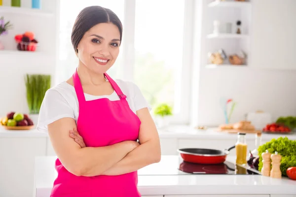 Фотопортрет жінки в рожевому фартусі, посміхаючись схрещеними руками на кухні — стокове фото