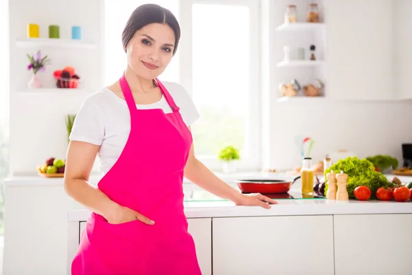 Фотопортретна жінка в рожевому фартусі посміхається на білій кухні вдома — стокове фото