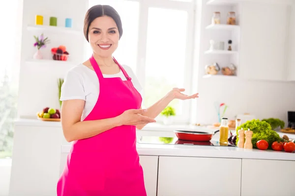 Фото чарівної милої зрілої жінки, одягненої в рожевий фартух, запрошує вас на кухню в приміщенні домашньої кімнати будинку — стокове фото