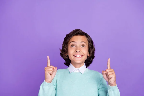 Foto von funky charmante Schuljunge tragen türkisfarbenen Pullover lächelnd zeigt nach oben suchen leeren Raum isoliert violette Farbe Hintergrund — Stockfoto