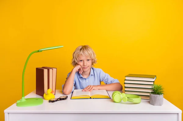 面白い疲れた学校の少年の写真青いシャツを着て座っているテーブルには多くのホームタスクがあります孤立した黄色の背景 — ストック写真