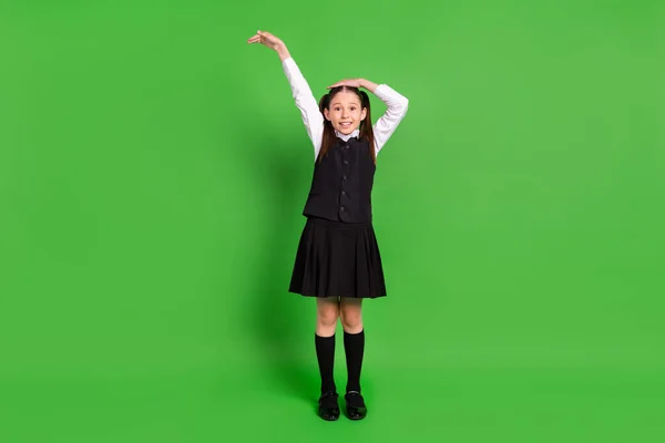 Foto de niña de la escuela bastante brillante usar negro blanco uniforme brazo de medición espacio vacío sonriendo aislado color verde fondo —  Fotos de Stock