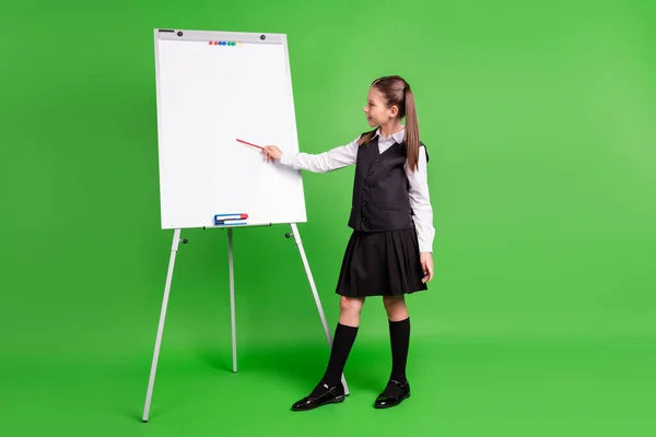 Φωτογραφία από γοητευτικό όμορφο κορίτσι σχολείο φορούν μαύρο λευκό στολή δείχνει λευκό πίνακα κενό χώρο χαμογελώντας απομονωμένο πράσινο χρώμα φόντο — Φωτογραφία Αρχείου