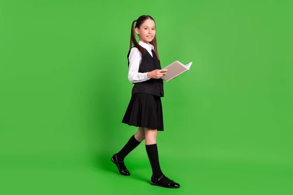 Foto von charmanten hübschen Schulmädchen tragen schwarze weiße Uniform zu Fuß Lesebuch lächelnd isoliert grüne Farbe Hintergrund — Stockfoto