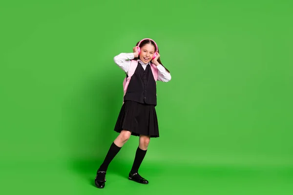 Foto di brillante divertente studentessa vestita bianco nero uniforme zaino auricolari sorridente canto isolato colore verde sfondo — Foto Stock