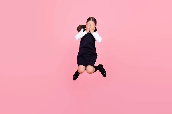 Full length body size photo schoolgirl jumping up covering face with hands isolated pastel pink color background — Stock Photo, Image