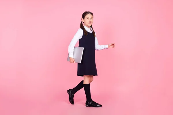 Full length body size photo schoolgirl in uniform walking on lesson keeping laptop isolated pastel pink color background — Stock Photo, Image