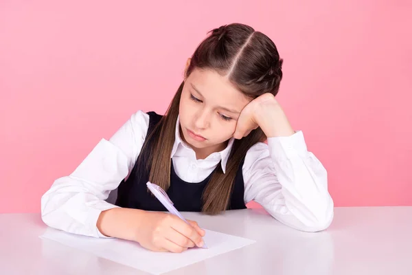 Foto retrato niña con colas sentado en el escritorio en la escuela prueba de escritura aislado pastel color rosa fondo — Foto de Stock