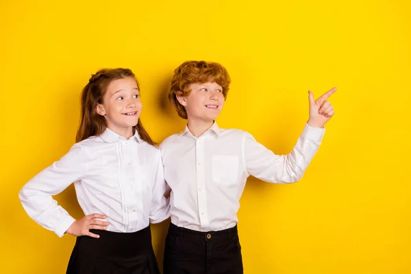 Фото двух мечтательных улыбающихся школьников, смотрящих рекламный продукт, обнимающих друг друга на желтом фоне — стоковое фото