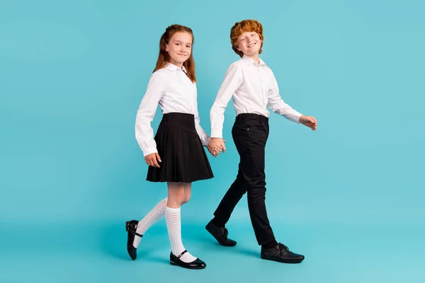 Comprimento total perfil de tamanho do corpo vista lateral de duas crianças alegres indo de mãos dadas lição isolada sobre fundo de cor azul brilhante — Fotografia de Stock